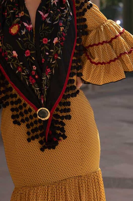 traje flamenca mostaza con lunares negros y detalles en las mangas rojo con mantoncillo negro con flores rojas
